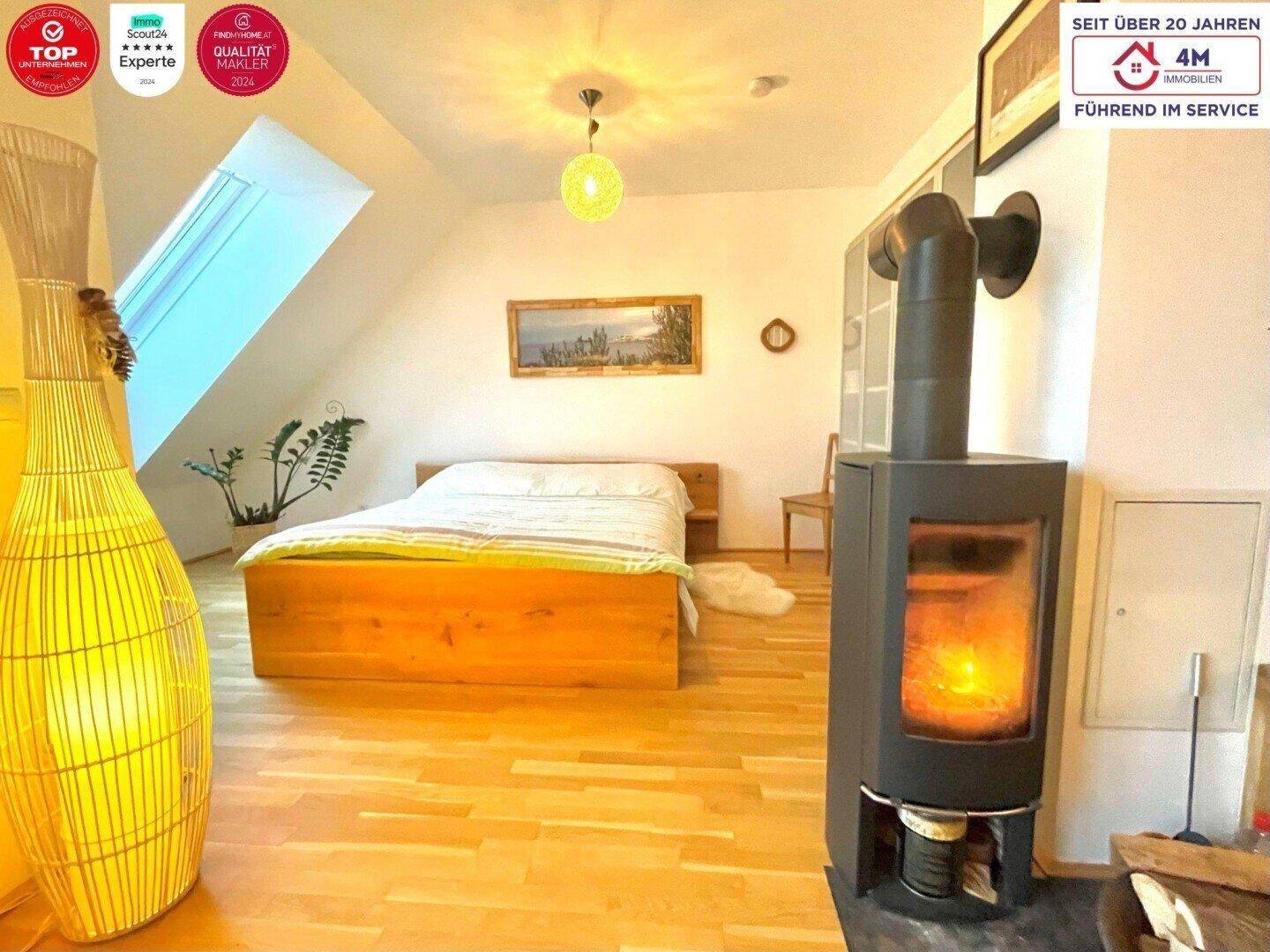 Schlafzimmer mit Holzbett, Kaminofen und Dachfenster, das viel natürliches Licht hereinlässt.