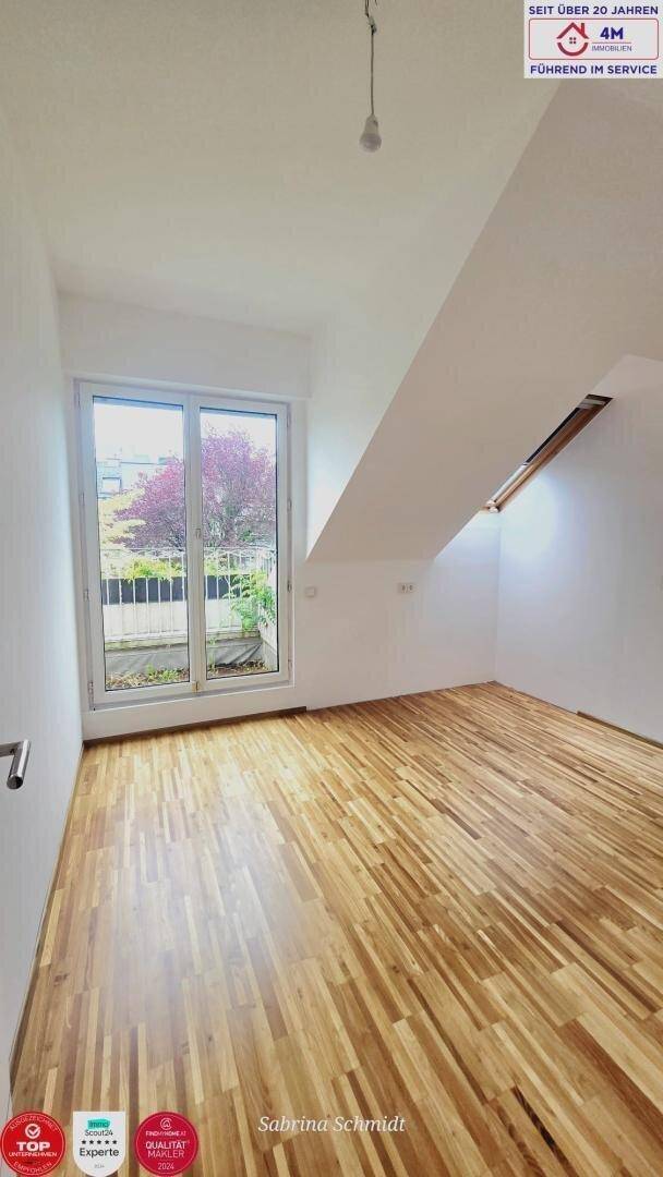 Leerer Raum im Dachgeschoss mit Holzboden und französischem Balkon mit Blick ins Grüne.