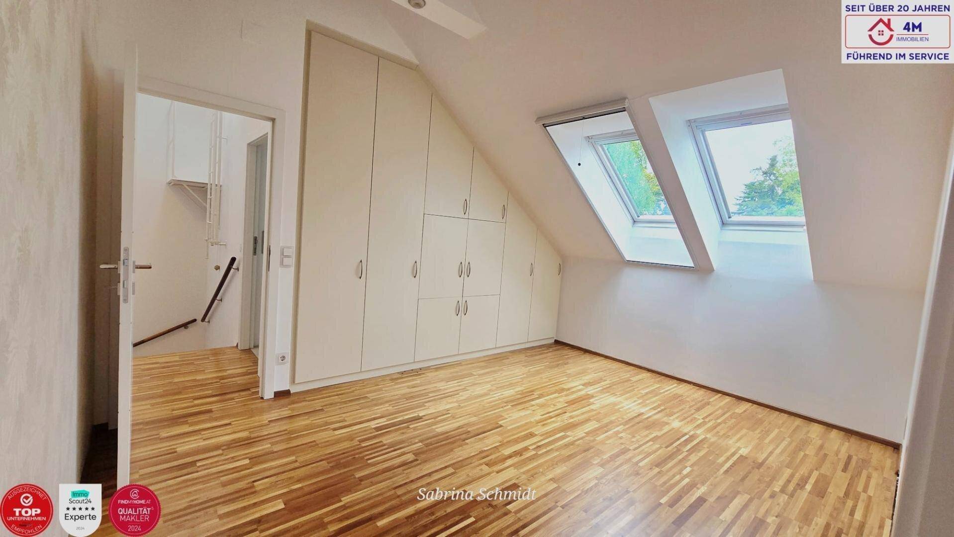 Heller Dachgeschossraum mit Einbauschränken, Holzboden und zwei Dachfenstern.