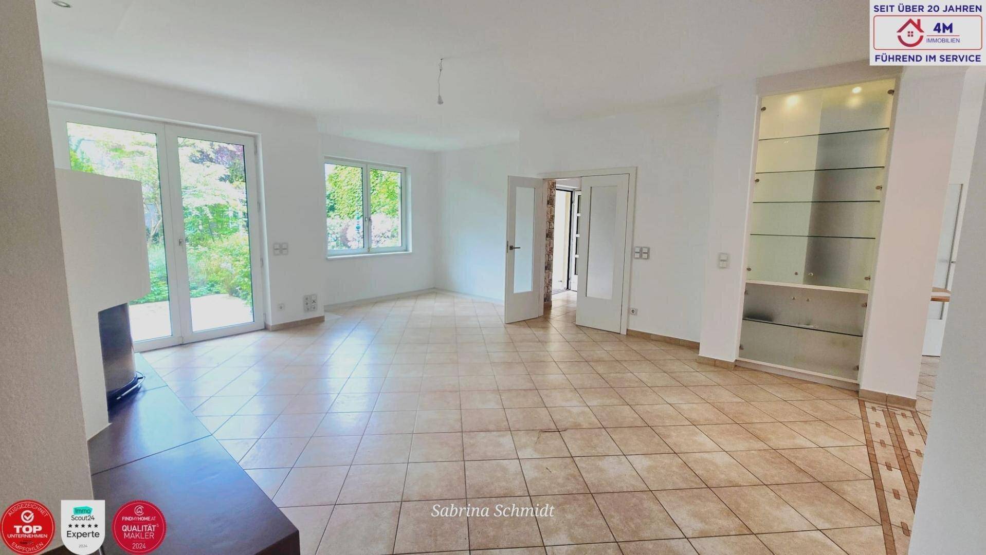 Geräumiger Wohnbereich mit Fliesenboden und Zugang zur Terrasse mit Gartenblick.