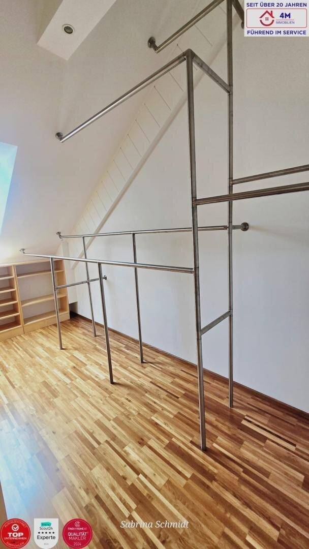 Begehbarer Kleiderschrank im Dachgeschoss mit Holzboden und Metallkleiderstangen.