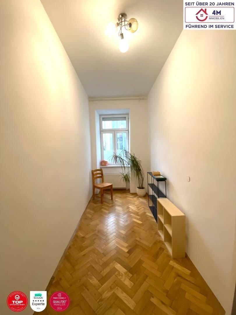 Langer Flur mit Fischgrätparkett, Fenster und einfacher Einrichtung.