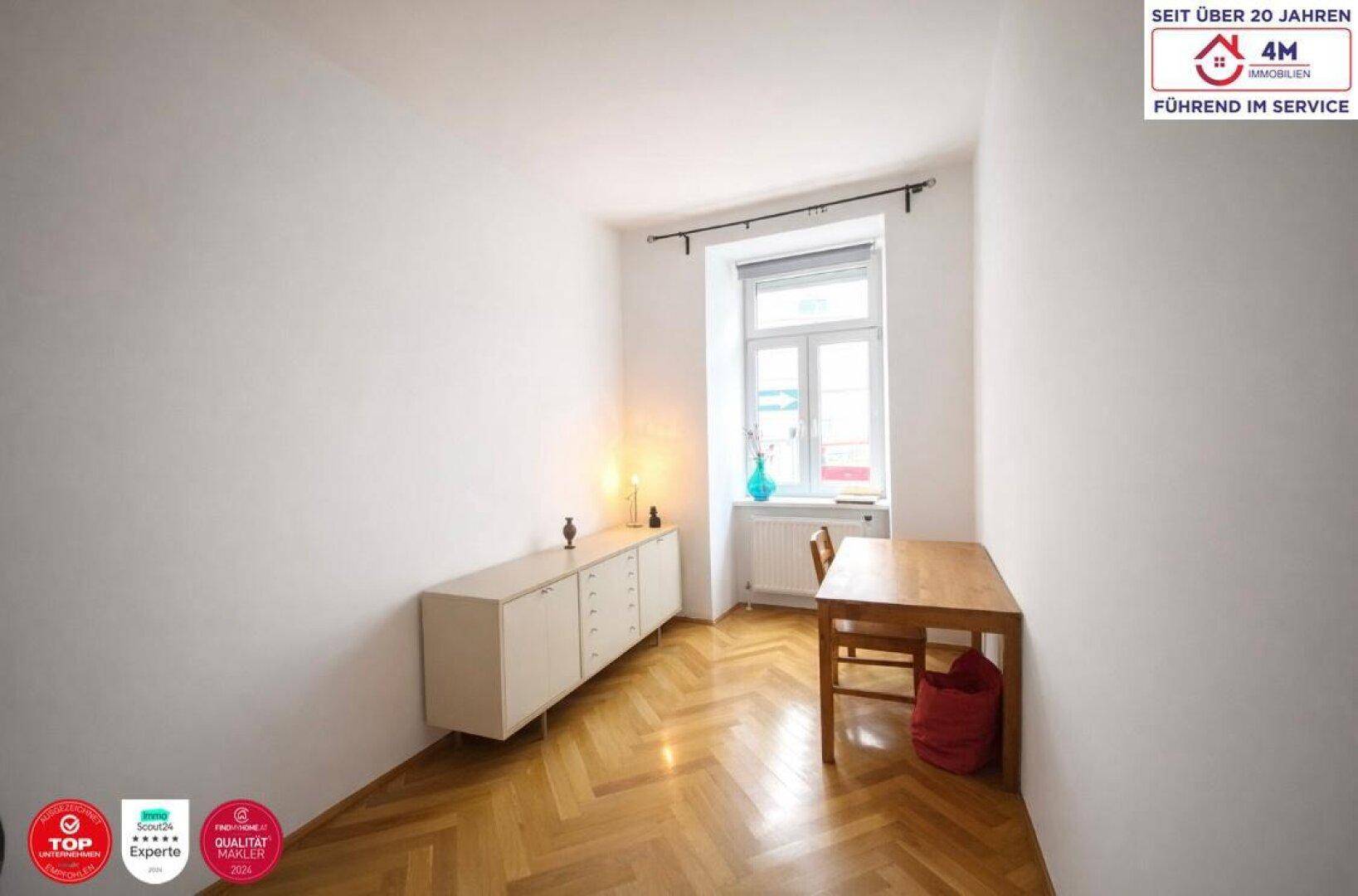 Kleiner Raum mit Fischgrätparkett, Fenster und schlichten Möbeln.