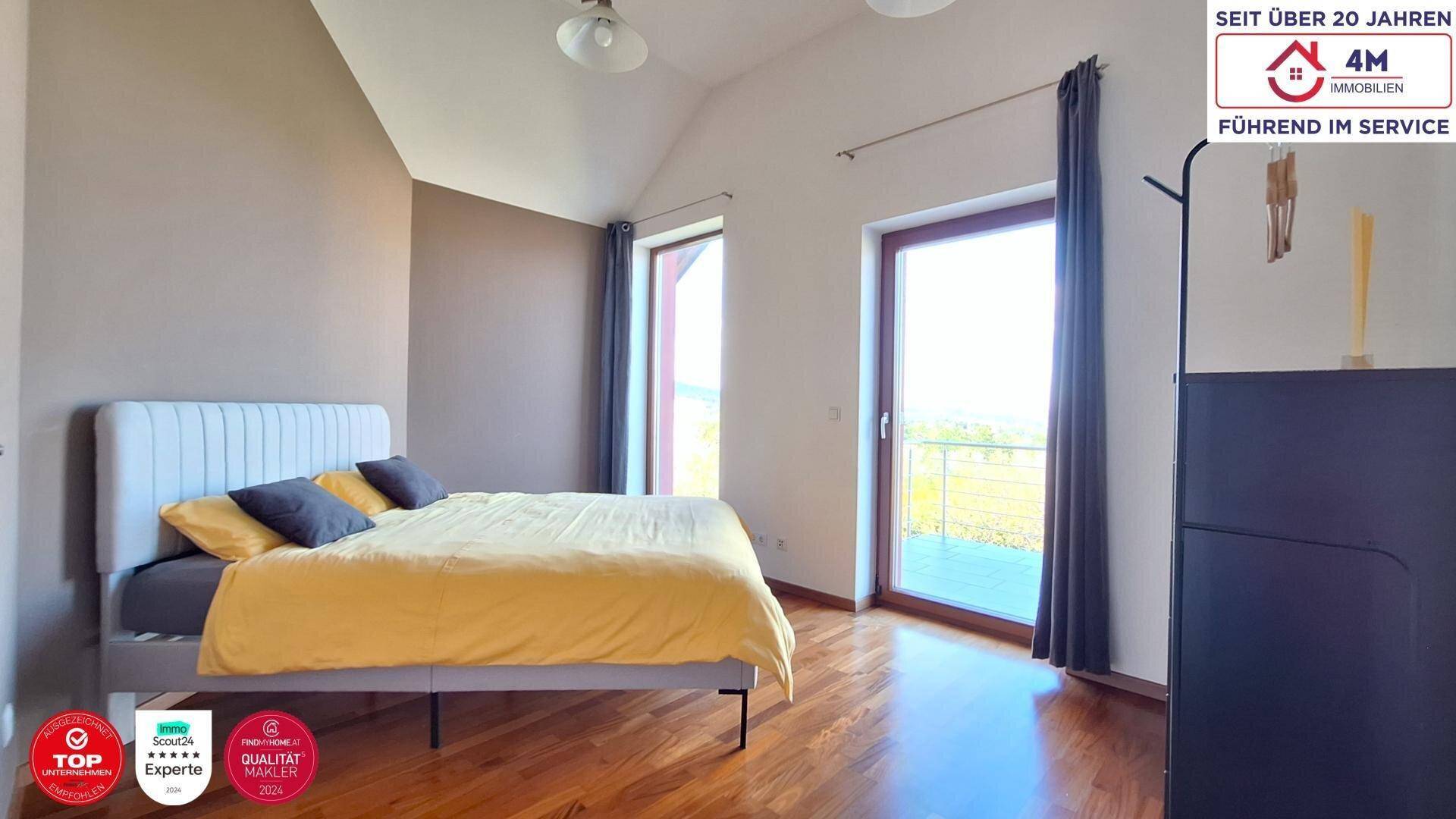 Helles Schlafzimmer mit Holzboden, Dachschräge und zwei großen Fenstern für viel Tageslicht.