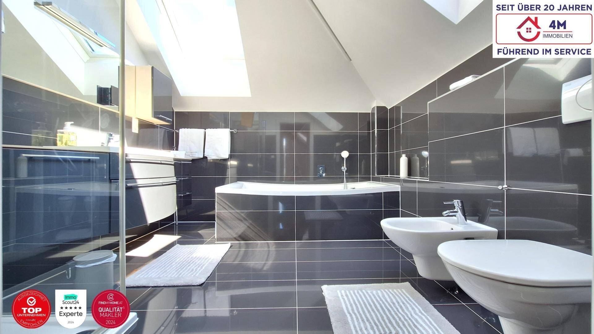 Modernes Badezimmer mit dunklen Fliesen, Eckbadewanne, Bidet und einem Dachfenster für Tageslicht.