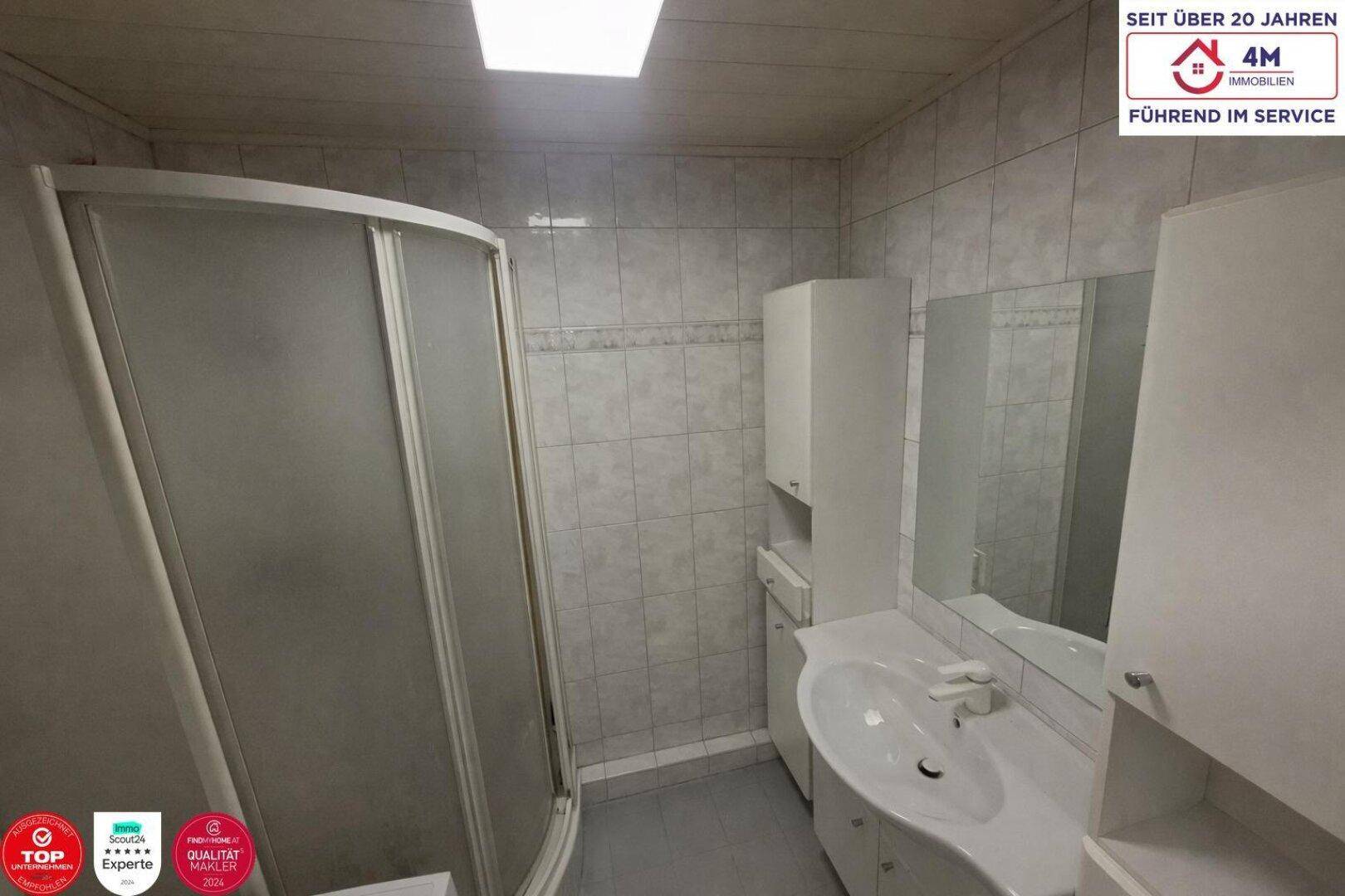 Badezimmer mit Eckdusche, Einzelwaschbecken und weißen Fliesen an Wänden und Boden.