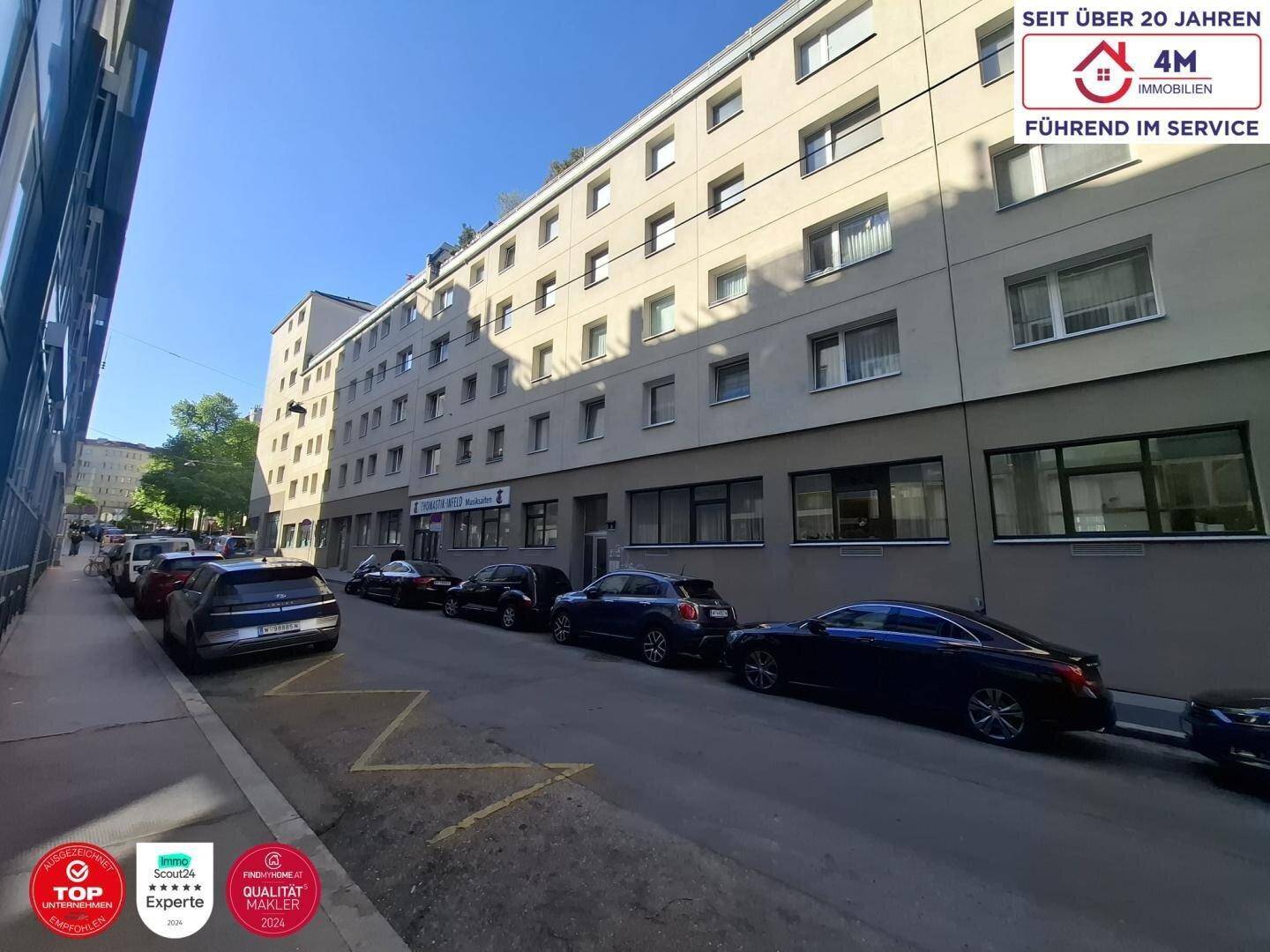 Mehrstöckiges Wohngebäude mit vielen Fenstern und geparkten Autos auf der Straße.
