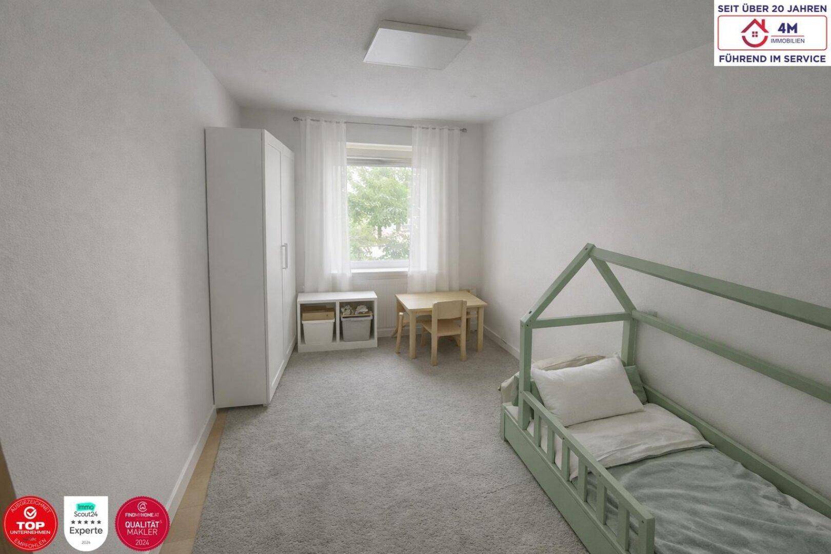 Kinderzimmer mit hellem Bett, weißem Kleiderschrank und kleinem Tisch am Fenster.
