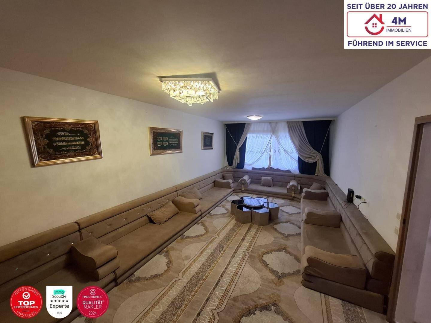 Traditionell eingerichtetes Wohnzimmer mit orientalischem Teppich, niedrigen Sitzgelegenheiten und dekorativen Bildern.