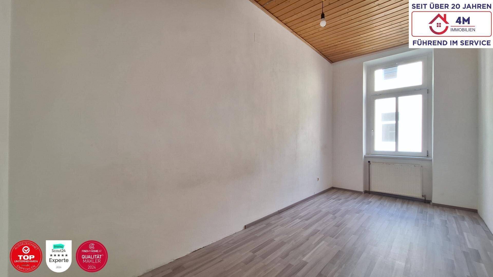 Geräumiges Zimmer mit Holzbalkendecke, Laminatboden und einem großen Fenster, ideal für individuelle Gestaltung.