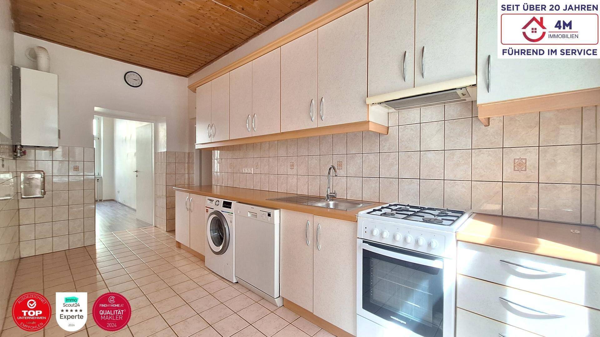 Funktionale Küche mit weißen Schränken, Gasherd, Spüle und Waschmaschine, auf gefliestem Boden.