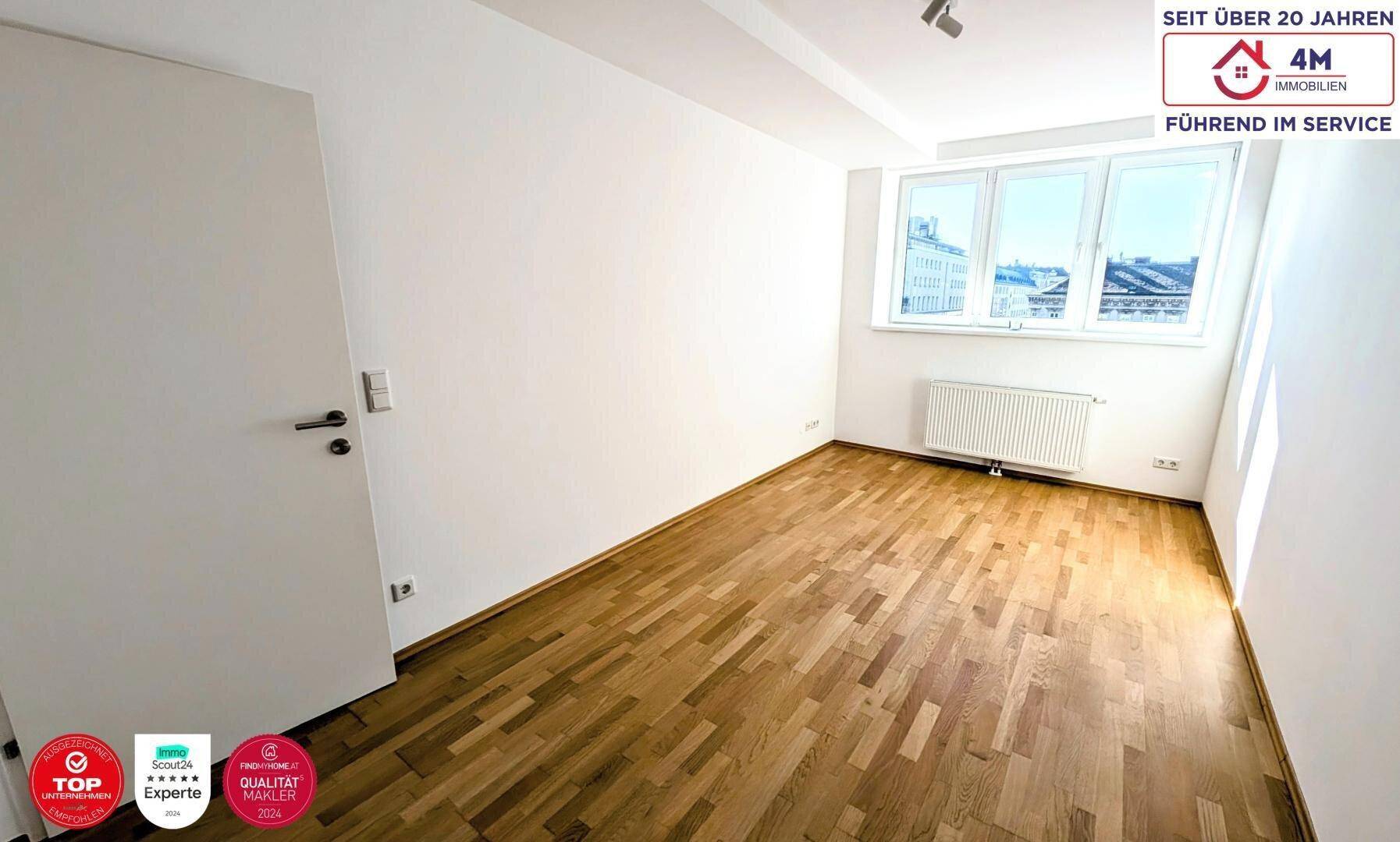 Helles Schlafzimmer mit Parkettboden, weißen Wänden und Blick auf die städtische Umgebung.