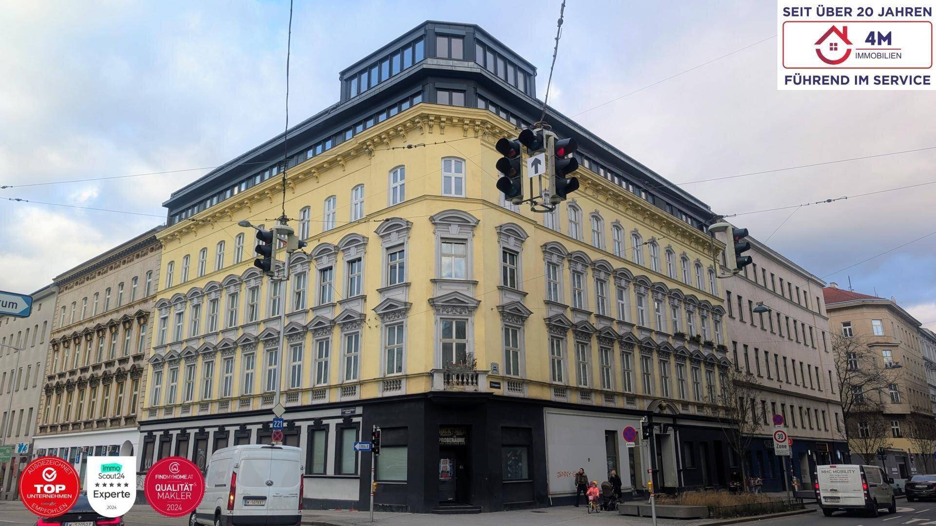 Historisches Eckgebäude mit gelber Fassade und modernen oberen Etagen an einer belebten Straße.