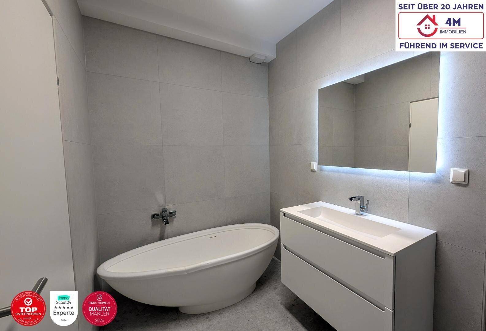 Elegantes Badezimmer mit freistehender Badewanne, modernem Waschtisch und beleuchtetem Spiegel.