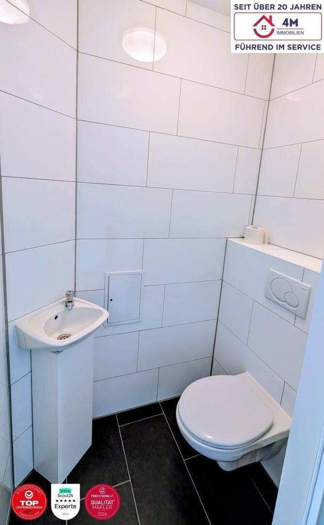 Kleines Gäste-WC mit weißen Fliesen, wandhängendem WC und kompaktem Eckwaschbecken.