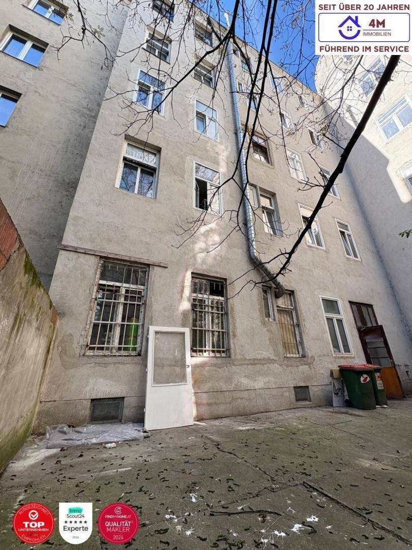 Rückseite eines alten Gebäudes mit vielen Fenstern und einem ungepflegten Hinterhofbereich.