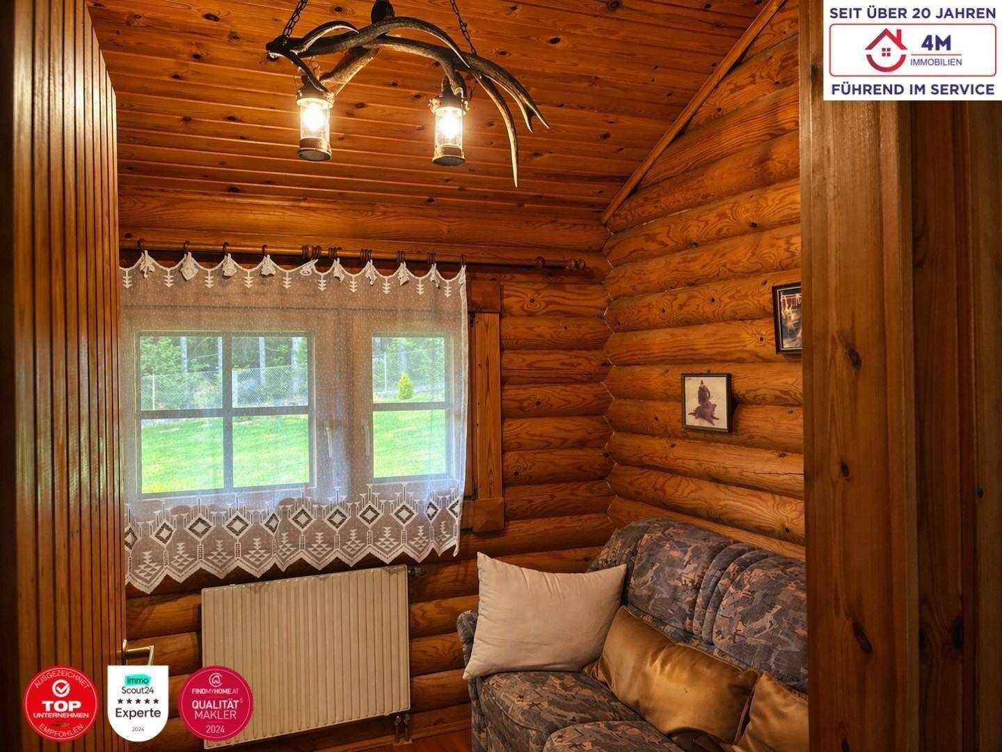 Gemütlicher Sitzbereich im Blockhausstil mit Holzwänden, Fenster und einem rustikalen Geweihleuchter.