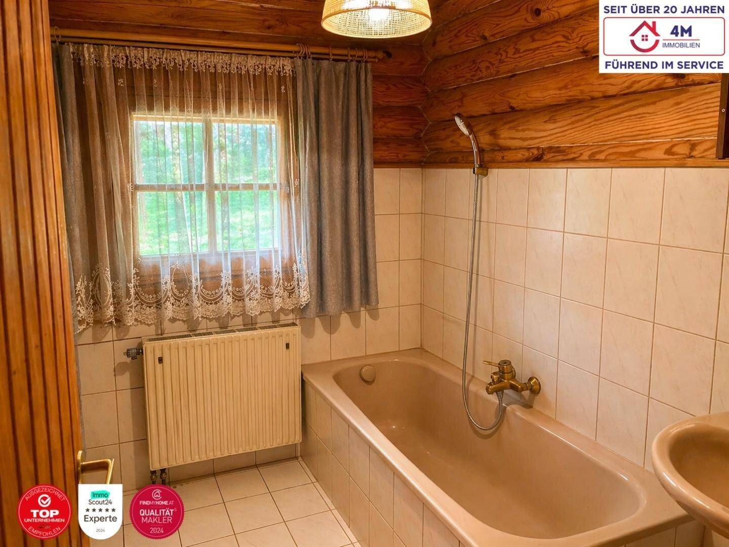 Badezimmer im rustikalen Stil mit Badewanne, Waschbecken, Heizkörper und Fenster, teilweise Holzverkleidung.