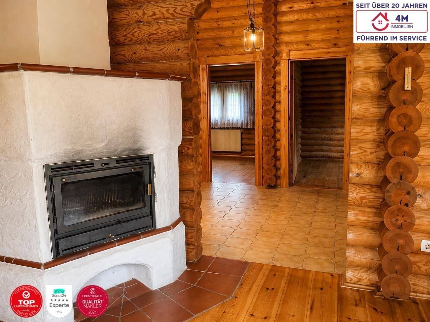Blick auf den Kamin im Blockhaus-Wohnzimmer mit angrenzenden Räumen und unterschiedlichen Bodenbelägen.