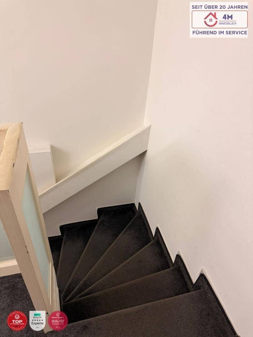 Schmale Treppe mit Teppichboden und schlichtem Holzgeländer, die in ein Obergeschoss führt.