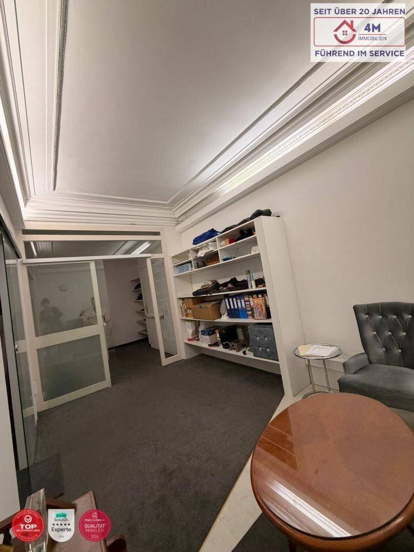 Büroraum mit Regalsystem, runden Tischen und Stühlen, durch eine Glastür zugänglich.
