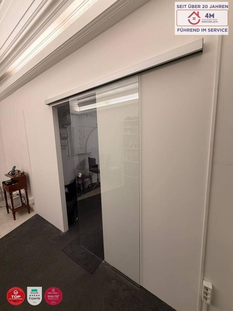 Eingangsbereich eines Büros mit moderner Glasschiebetür und schlichten weißen Wänden.