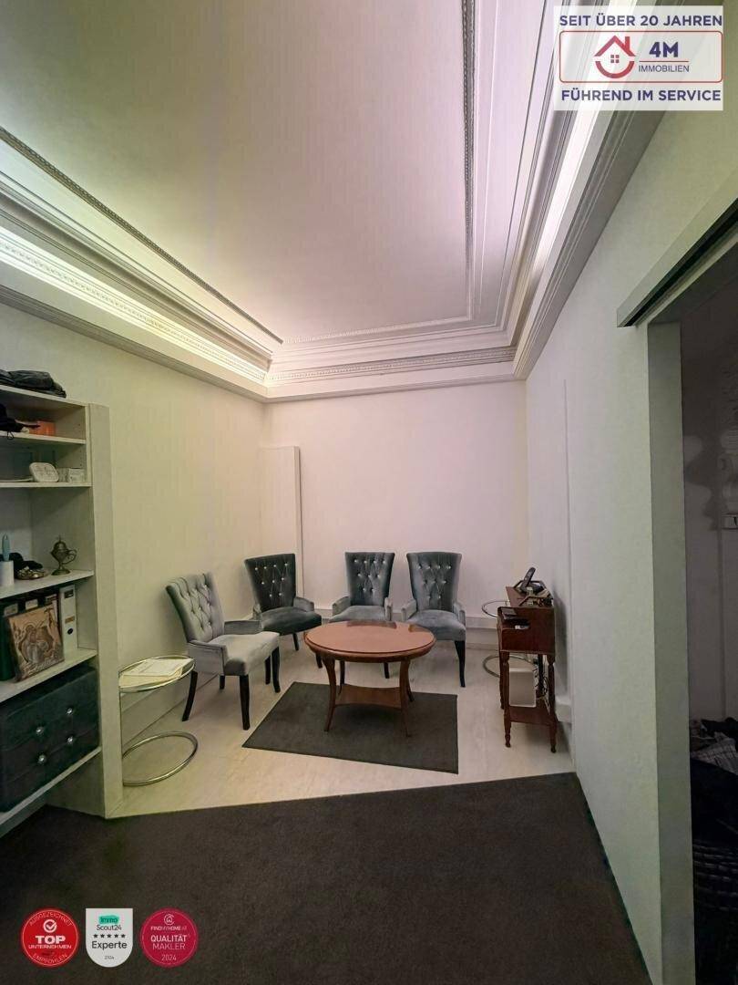Büroraum mit eleganten Stühlen, einem runden Tisch und dekorativen Deckenleisten.