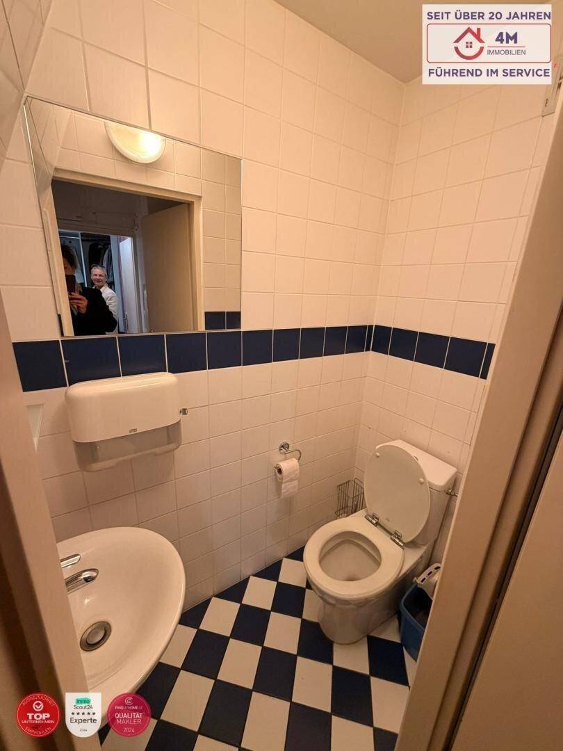 Kleines WC mit blau-weiß gefliesten Wänden und Boden, Waschbecken und Spiegel.
