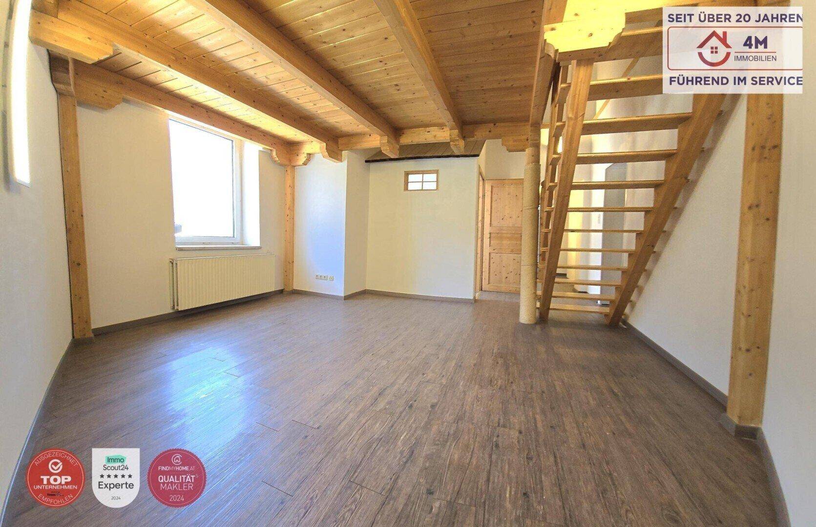 Geräumiger Wohnbereich mit Holzbalkendecke, Laminatboden und Holztreppe zum Obergeschoss.