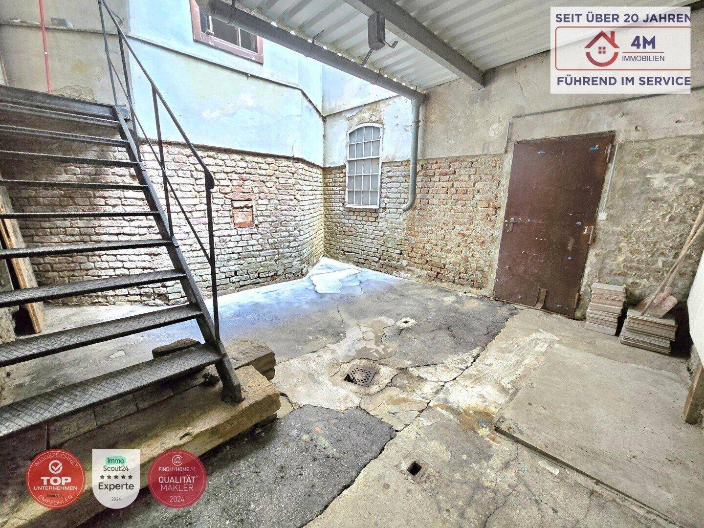 Großer Kellerraum mit rohen Ziegelwänden, Betonboden und Metalltreppe.