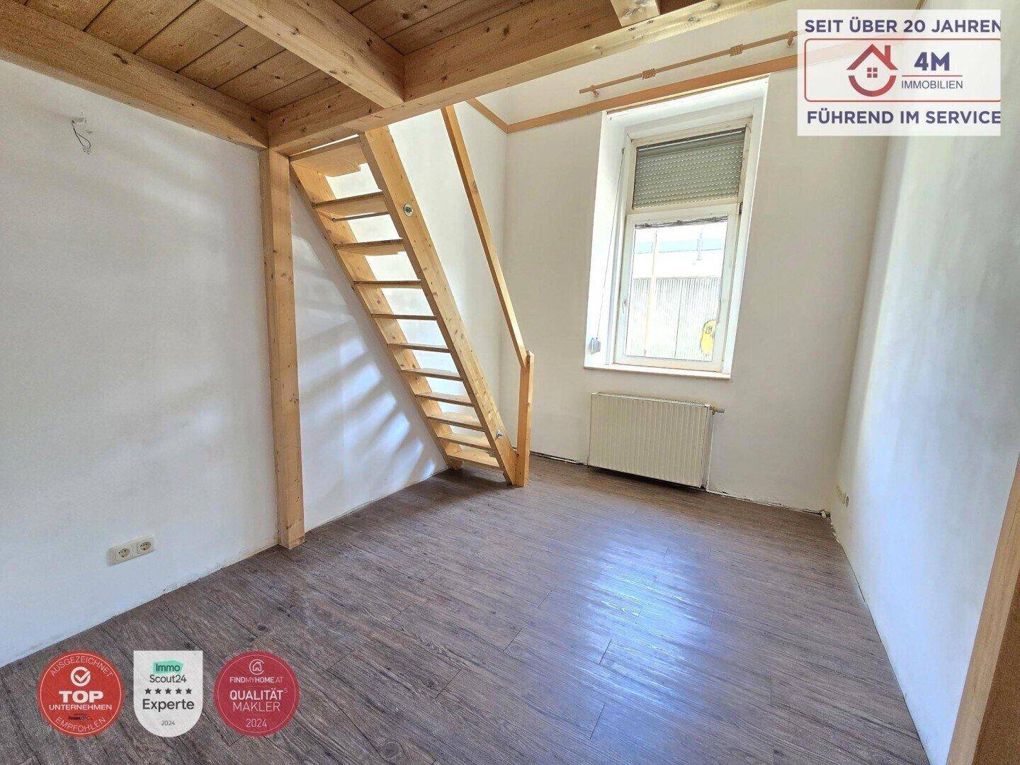 Heller Raum mit Laminatboden, Fenster und Holztreppe zu einem erhöhten Bereich.