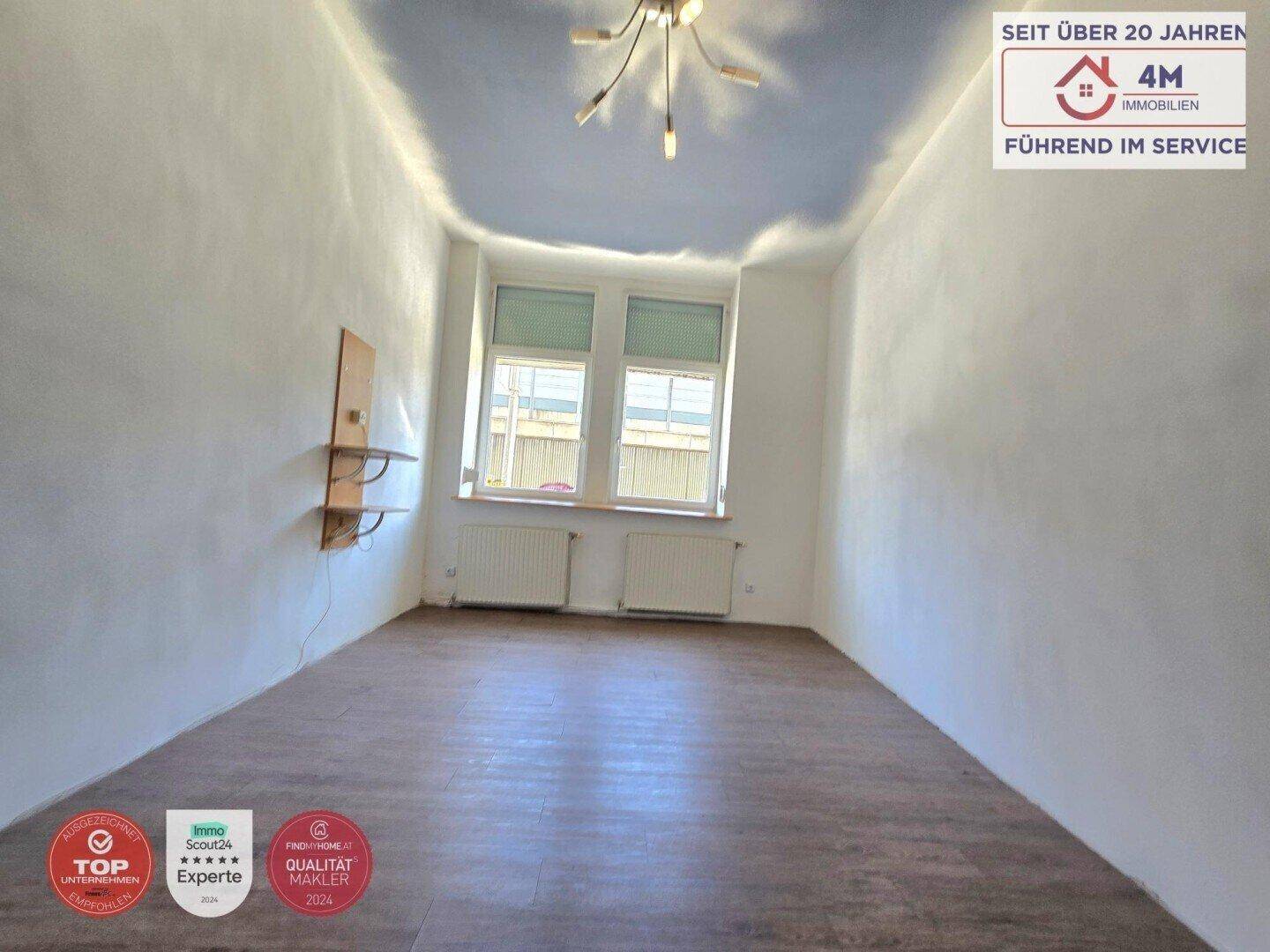 Heller Raum mit Laminatboden, zwei Fenstern und einer Decke mit dekorativer Malerei.
