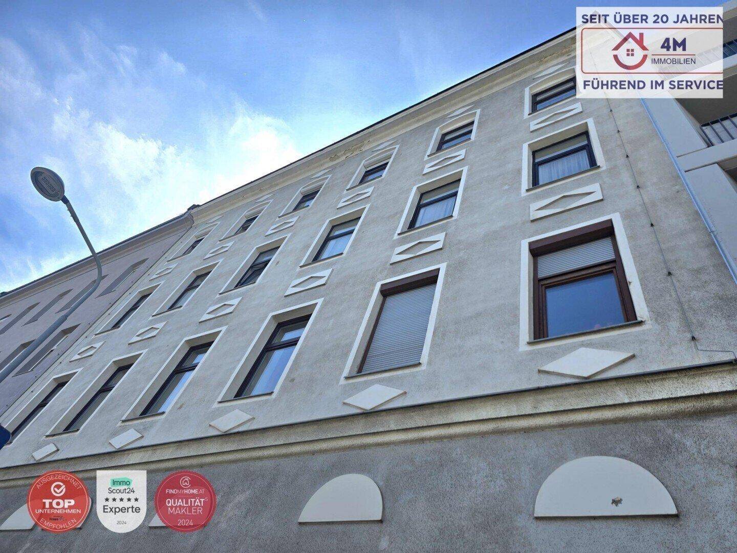 Klassische Fassade eines Mehrfamilienhauses mit mehreren Fenstern und dekorativen Elementen.