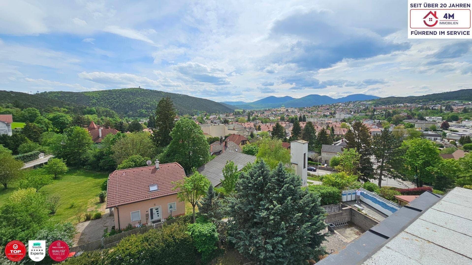 Panoramablick über eine grüne Stadtlandschaft mit umliegenden Hügeln und Bergen.