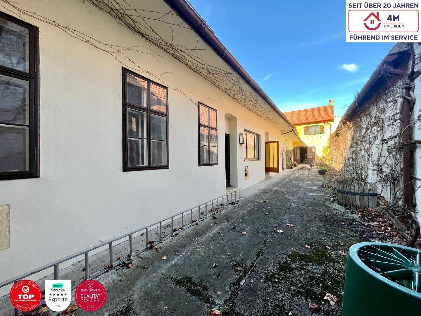 Langer gepflasterter Hof zwischen Gebäuden mit natürlicher Begrünung, bietet viel Platz im Freien.