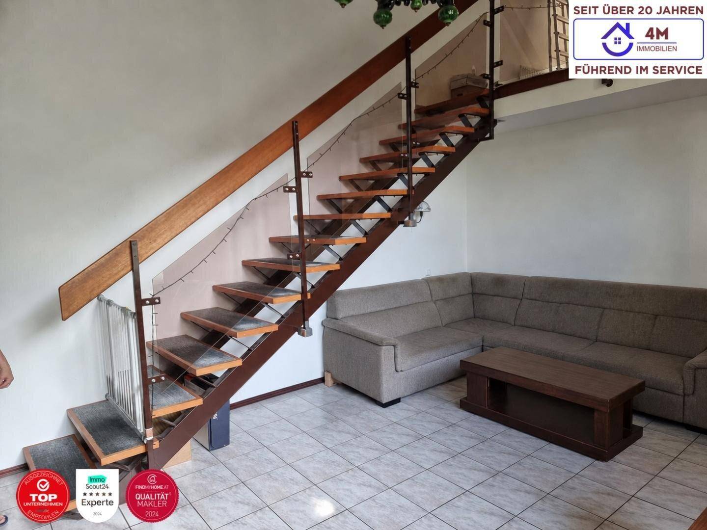 Wohnbereich mit offener Treppe, Fliesenboden und einem beigen Ecksofa.