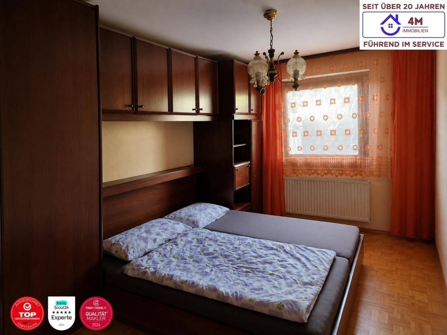 Schlafzimmer mit Einbauschrank, Doppelbett und Fenster mit orangefarbenen Vorhängen.