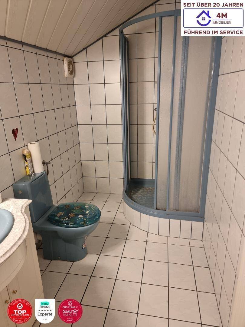 Badezimmer mit blauer Toilette, Duschkabine und weißen Fliesen an Wänden und Boden.
