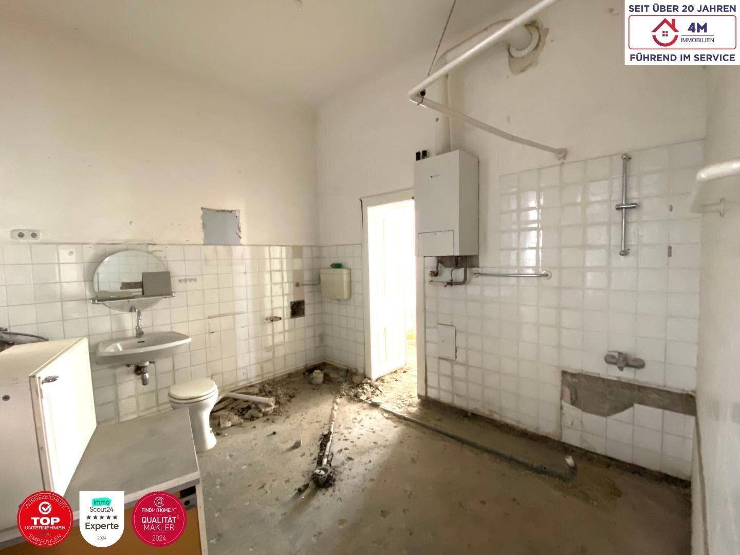 Badezimmer im Rohzustand mit alten Fliesen, Toilette und Waschbecken, bereit zur Sanierung.