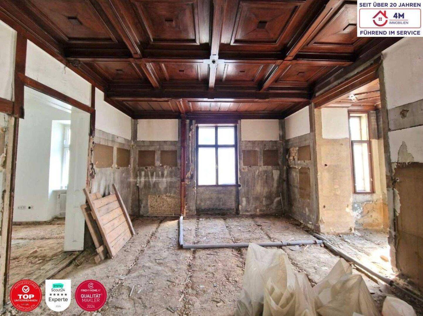 Großer Raum im Rohzustand mit beeindruckender Kassettendecke aus Holz, bereit zur Umgestaltung.