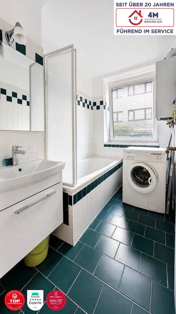 Badezimmer mit Badewanne, Duschabtrennung, Waschbecken und Waschmaschine, hell gefliest.