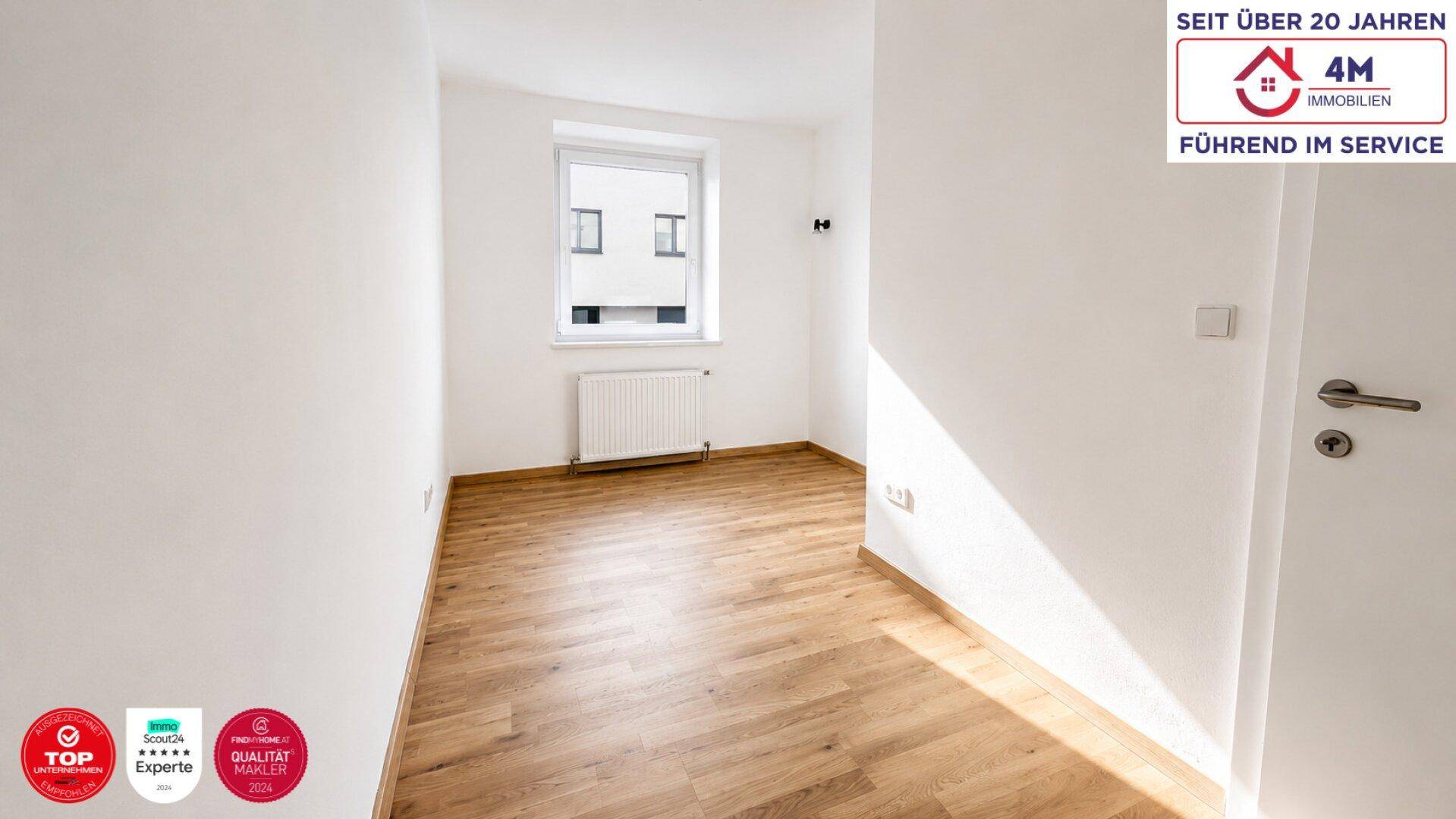 Leeres Zimmer mit Holzboden, weißen Wänden und einem Fenster für natürliches Licht.