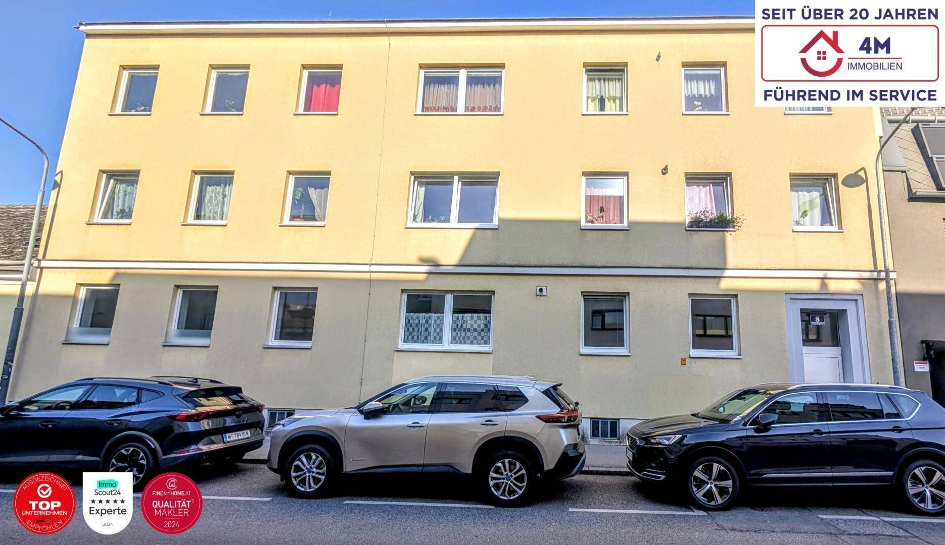 Mehrstöckiges Wohngebäude mit gelber Fassade und geparkten Autos davor.