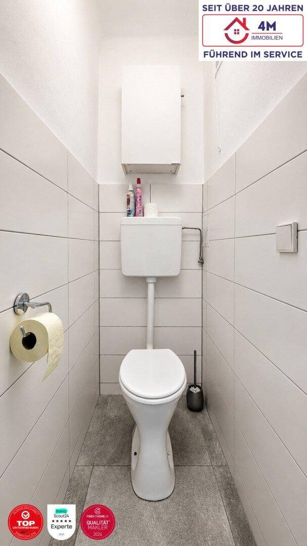 Separates WC mit Toilette, weißen Wandfliesen und grauem Boden.