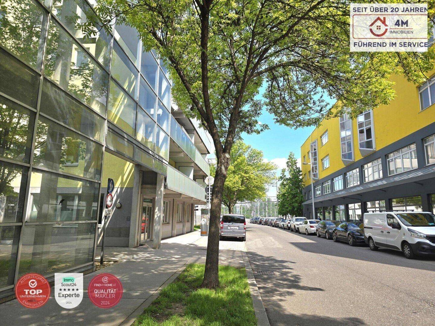 Außenansicht der Wohnanlage mit Bäumen, geparkten Autos und moderner Architektur.