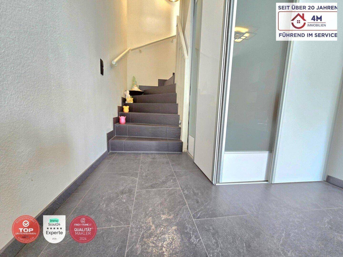 Heller Flur mit Treppe zum Obergeschoss und modernem Fliesenboden.