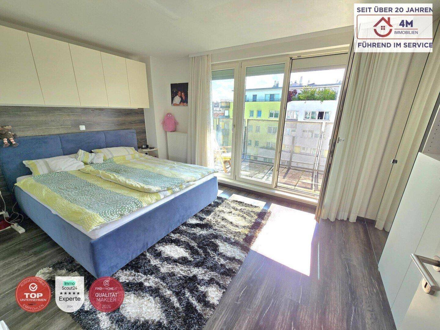 Helles Schlafzimmer mit modernem Bett, Laminatboden und direktem Zugang zu einem Balkon.