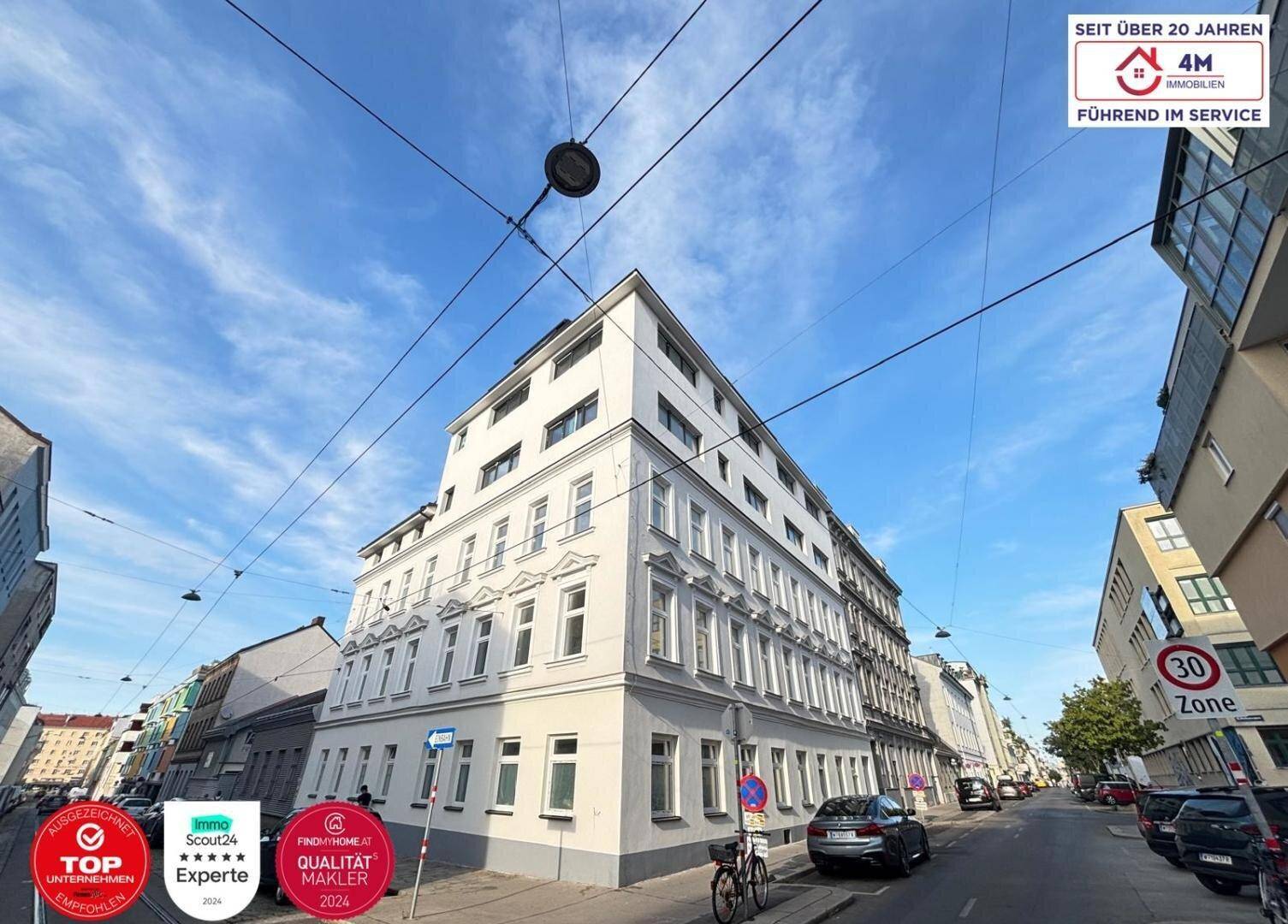 Außenansicht eines Eckgebäudes an einer Stadtstraße unter blauem Himmel.