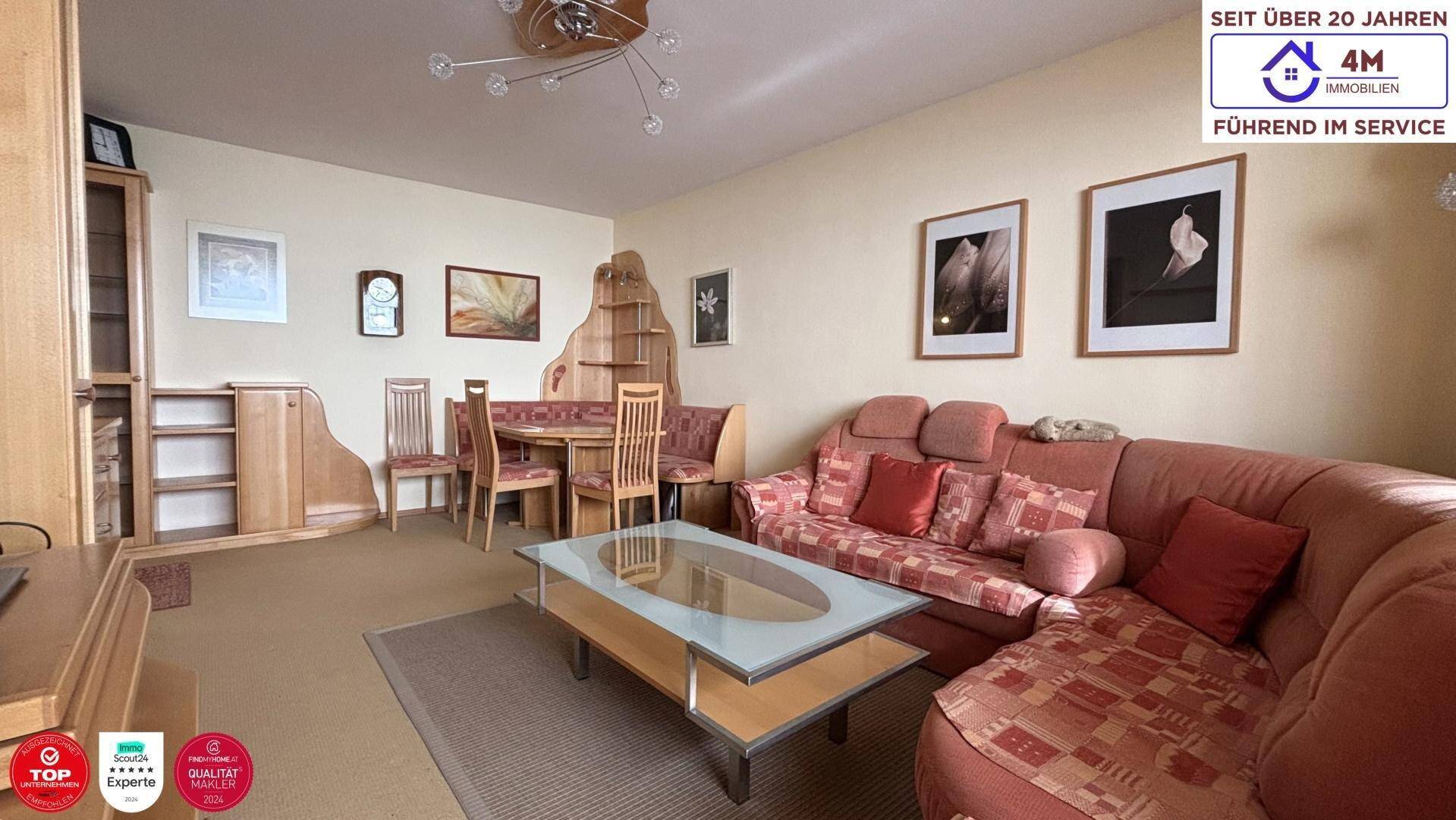 Heller Wohn- und Essbereich mit beigem Teppichboden, rotem Sofa und Holzmöbeln.