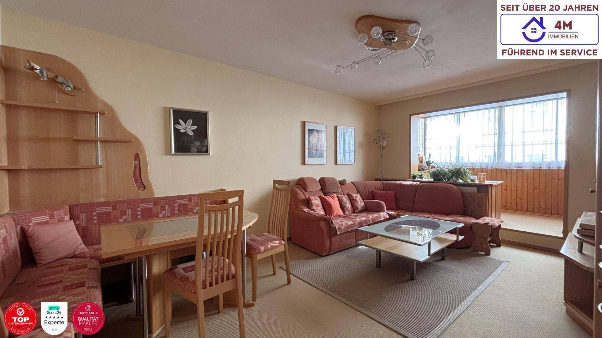 Gemütlicher Wohn- und Essbereich mit rotem Sofa, Esstisch und Zugang zu einem verglasten Balkon.